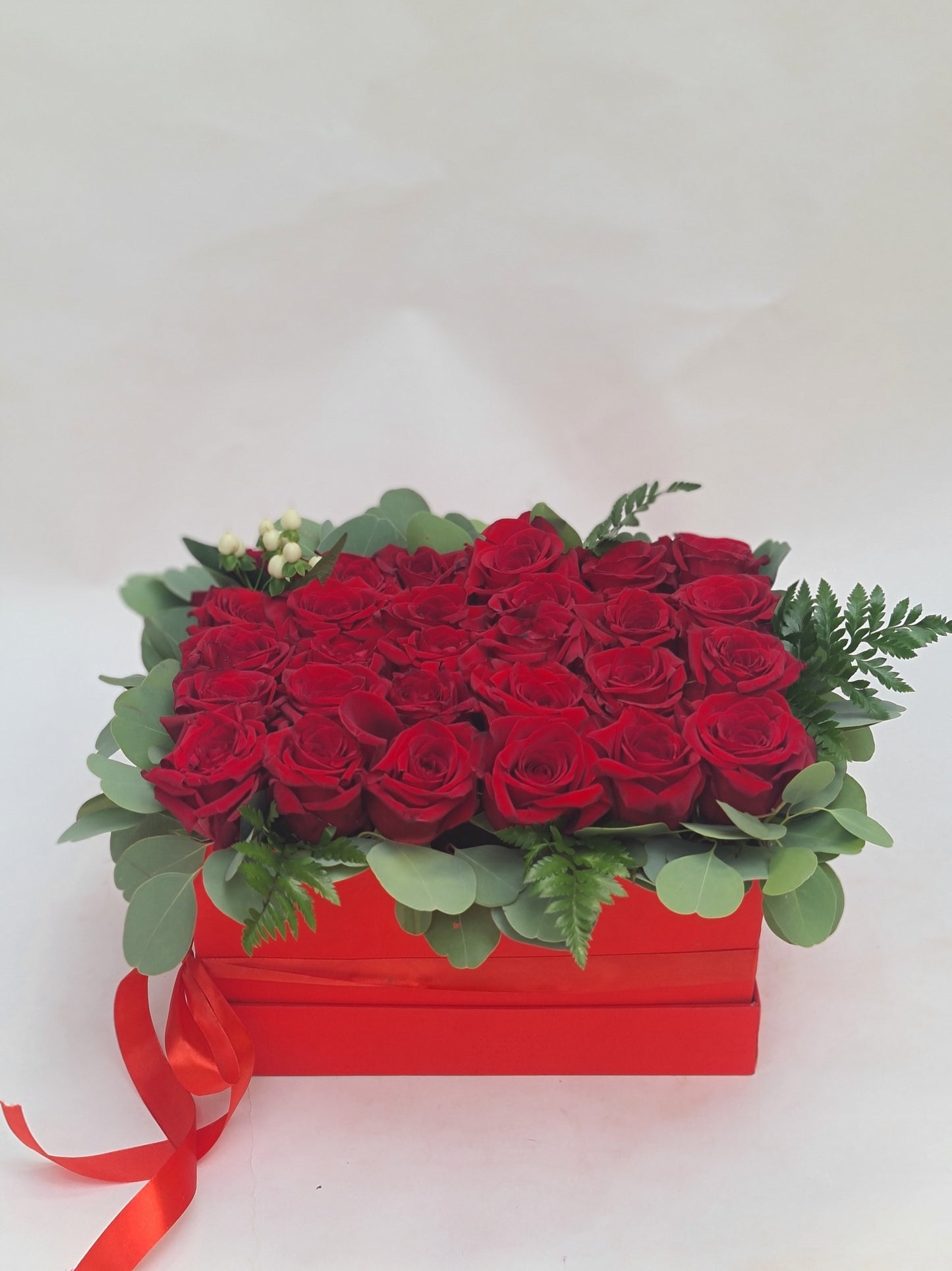 BOX OF RED ROSES WITH GREEN FILLERS.
